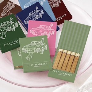 May include: A collection of rectangular matchboxes in various colors including green, blue, pink, and brown. Each box features a white line drawing of a convertible car with the text A+T on the license plate and the words JUST MARRIED below.