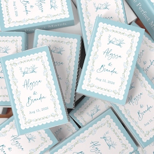May include: A collection of light blue matchboxes with white scalloped edges and floral designs. Each box features the names "Alyssa & Brandon" and the date "Aug 15, 2026", along with a bird illustration, perfect for a wedding.