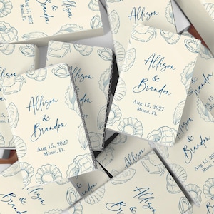 May include: Off-white wedding favor boxes with a blue seashell design. The boxes are printed with the names "Allison & Brandon", the date "Aug 15, 2027", and the location "Miami, FL". The boxes are scattered.
