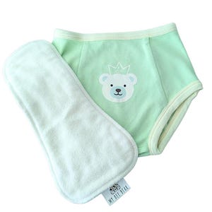 May include: A light green baby training pant with a white absorbent insert. The training pant features a bear graphic wearing a crown. The absorbent insert is white and rectangular. The brand name "MY BEE BEAR" is on a small tag.
