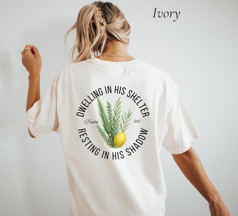 May include: Ivory-colored t-shirt with a circular graphic on the back. The graphic features green leaves, a yellow lemon, and the text "Dwelling in His Shelter, Resting in His Shadow, Psalm 91:1."