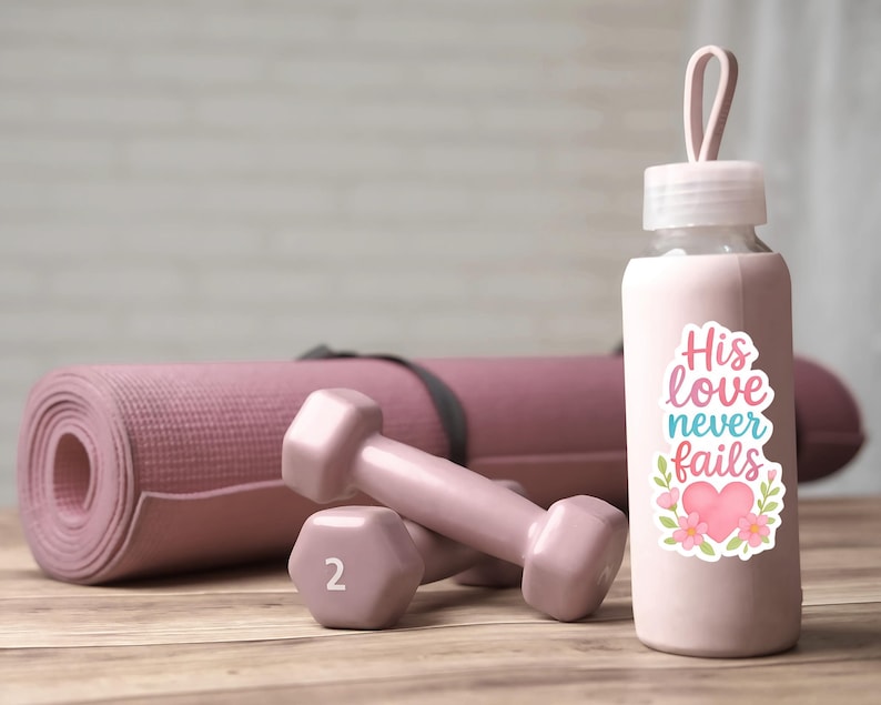May include: A pink water bottle with a sticker that reads "His love never fails" next to two pink 2-pound dumbbells and a rolled-up yoga mat. The items are on a wooden surface.