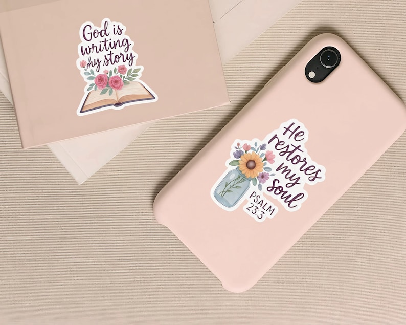 May include: Two stickers with religious quotes and floral designs. One sticker features the text "God is writing my story" above an open book with flowers. The other sticker says "He restores my soul" with a floral arrangement and the text "Psalm 23:3".