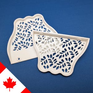 May include: Two white, leaf-patterned, decorative trays. The trays have a scalloped edge and a series of leaf-shaped cutouts. One tray has a small hole. The background is a solid blue.