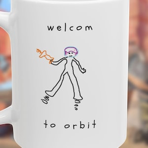 May include: A white ceramic mug featuring a black line drawing of a figure holding an orange object, with the text "welcom to orbit" printed in black. The figure has a pink circular head and stands on two small spring-like shapes.