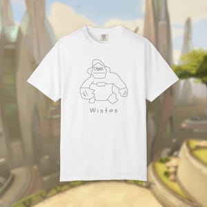 Peut inclure: Un t-shirt blanc à manches courtes orné d'un dessin au trait noir représentant un gorille portant des lunettes. Sous l'illustration, le mot Winton est imprimé dans une police simple et manuscrite. Le t-shirt a un col rond et une coupe standard.