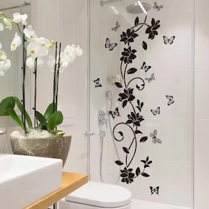 May include: A bathroom scene featuring a white orchid plant in a decorative pot, a white sink, and a shower with black floral and butterfly decals. The decals are applied to the glass shower door.