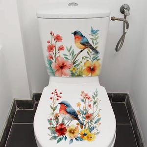 Könnte beinhalten: Weiße Toilette mit Blumen- und Vogeldesign. Der Toilettentank und der Sitz zeigen Aquarellillustrationen von bunten Vögeln, die auf Ästen sitzen, umgeben von Blumen in Rot-, Orange-, Gelb- und Blautönen.