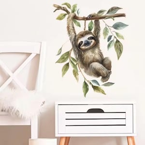 May include: A watercolour wall decal of a smiling sloth hanging from a tree branch with green leaves. The sloth is brown and tan, with a light-coloured face. The decal is designed for a nursery or children's room.