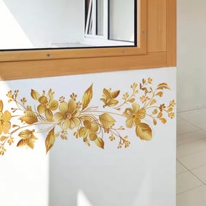 Peut inclure: Décoration murale florale dorée. Le motif floral détaillé, composé de fleurs et de feuilles, est appliqué sur un mur blanc, sous un cadre de fenêtre en bois. Idéal pour la décoration intérieure.