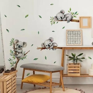 May include: Wall stickers showing cute koala bears on branches with green leaves. The koalas are in different poses, such as sleeping and clinging to branches. These stickers are designed to bring a playful and charming feel to any room.