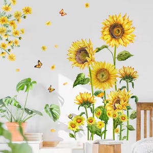 Op de afbeelding: Muurstickers met heldergele zonnebloemen, groene bladeren en oranje vlinders. De stickers vormen een vrolijk bloemstuk, met enkele zonnebloemen in volle bloei en andere in verschillende groeistadia. Een potplant is ook inbegrepen.