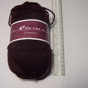 May include: A dark brown ball of Ella Rae Classic yarn. The yarn is wrapped with a burgundy label with white text. A ruler is placed next to the yarn, showing measurements in inches.