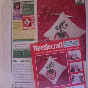 May include: A red and white Needlecraft starter pack for creating a scissor keeper. The kit includes instructions, embroidery floss, a needle, and calico fabric. The project features a strawberry design.