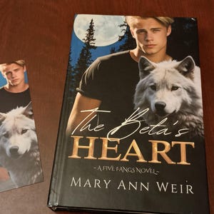 May include: A book cover with a black background and a white wolf. The title of the book is "The Beta's Heart" and the author is "Mary Ann Weir".