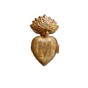 May include: A gold-colored heart-shaped pendant with a floral design on top and the letters "M" and "M" inside the heart.