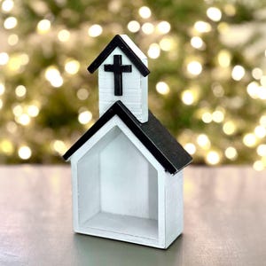 May include: A white wooden church with a black roof and a black cross on the steeple. The church is a small decorative item, ideal for a shelf or table.