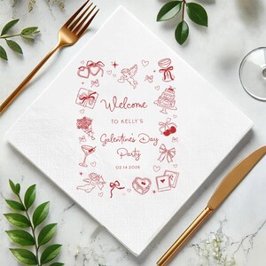 May include: White square paper napkin with red illustrations and text. The design includes hearts, gifts, and the words "Welcome to Kelly's Galentine's Day Party 02.14.2026". A gold fork and knife are on the sides.