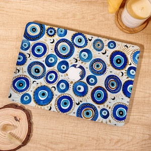 May include: A laptop skin featuring a repeating pattern of blue and white evil eye motifs. The design includes various sizes of concentric circles in shades of navy, light blue, and gold, interspersed with small black crescent moons and star shapes.