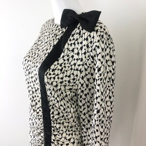 May include: A black and white patterned dress with a black bow on the shoulder. The dress has a long sleeve and a fitted silhouette.