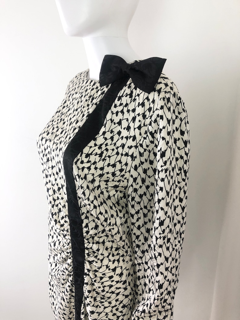 May include: A black and white patterned dress with a black bow on the shoulder. The dress has a long sleeve and a fitted silhouette.