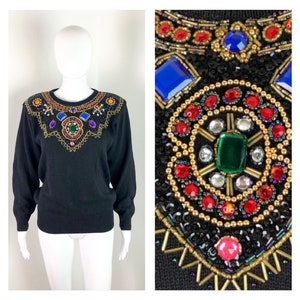 May include: Black sweater with a large, colourful, beaded and sequined design on the neckline. The design features a variety of colours, including red, green, blue, and gold.