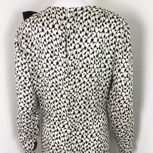 May include: A white and black patterned long-sleeved dress with a black bow at the neckline.