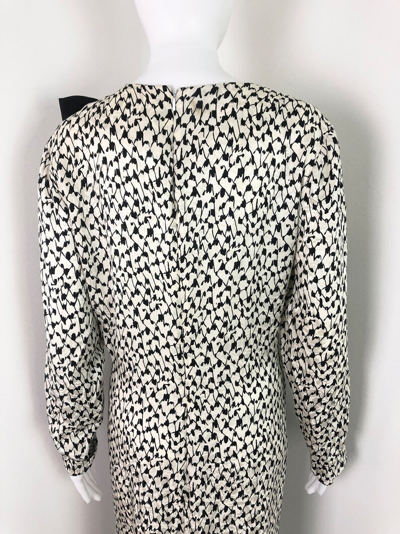 May include: A white and black patterned long-sleeved dress with a black bow at the neckline.