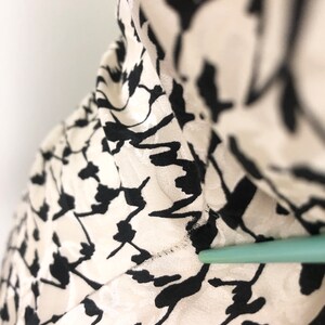 May include: Close-up of a white and black patterned fabric. The fabric has a textured surface and a subtle sheen.
