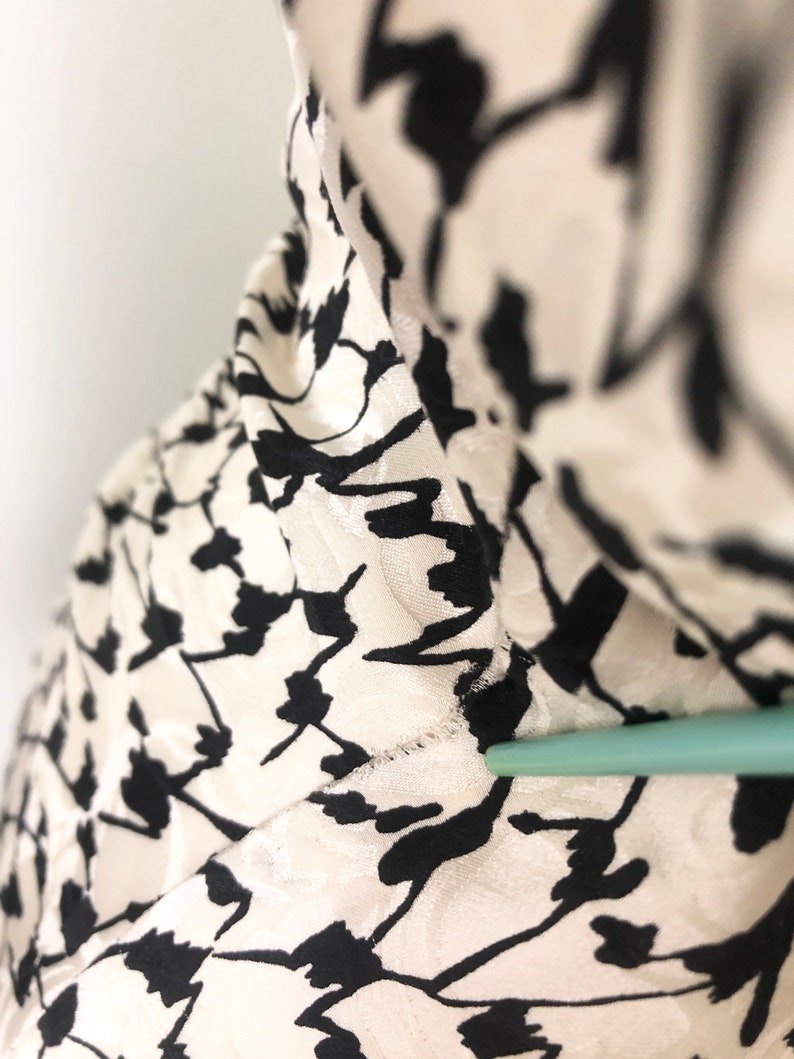 May include: Close-up of a white and black patterned fabric. The fabric has a textured surface and a subtle sheen.