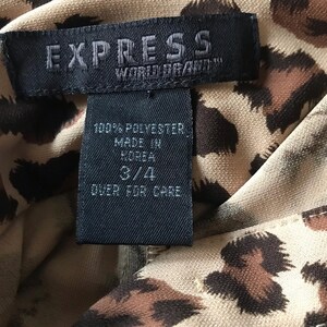 May include: A black and white tag with the text "EXPRESS WORLD BRAND" and "100% POLYESTER MADE IN KOREA 3/4 OVER FOR CARE" on a brown and tan leopard print fabric.