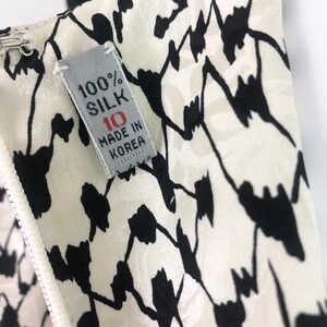 May include: A white silk fabric with a black floral pattern. The fabric has a label that reads "100% Silk" and "Made in Korea".