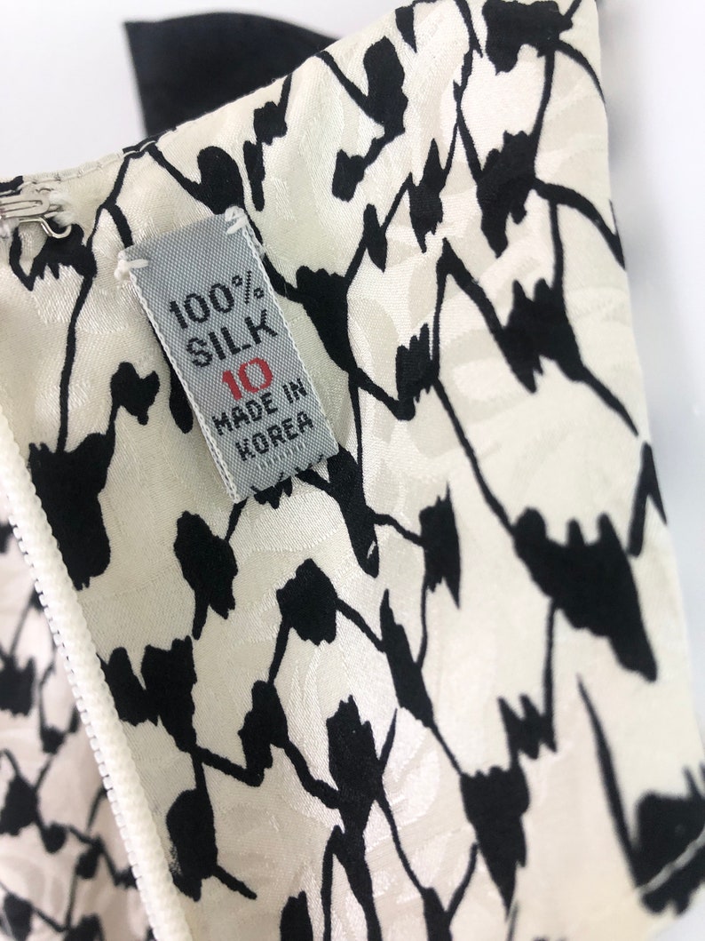 May include: A white silk fabric with a black floral pattern. The fabric has a label that reads "100% Silk" and "Made in Korea".