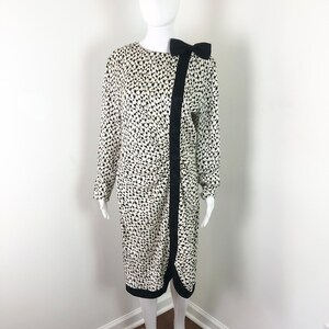 May include: A white dress with a black and white geometric print. The dress has a black bow at the neckline and a black trim around the hem.