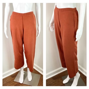 May include: A pair of wide-leg trousers in a burnt orange colour. The trousers have a straight leg and a relaxed fit.