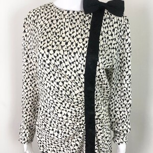 May include: A white and black patterned dress with a black bow at the shoulder. The dress has a long sleeve and a fitted silhouette.