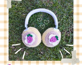 Pode incluir: Fones de ouvido brancos com capas de crochê. As capas são amarelo claro com um desenho de morango. A imagem inclui o texto "DIGITAL PATTERN" e "HOTCAKES HEADPHONE COVERS".