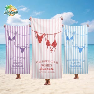 Puede incluir: Tres toallas de playa con rayas verticales en morado, rosa y azul. Cada toalla presenta un diseño de bikini y texto para una despedida de soltera. Las toallas se sostienen en una playa con cielo azul y océano al fondo.