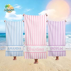 Peut inclure: Trois serviettes de plage rectangulaires à rayures verticales bleu clair, rose et lavande, chacune dotée d'une bande horizontale blanche unie sur la partie inférieure. Les noms AMANDA, Christina et ANDREW sont imprimés en blanc sur les bandes.
