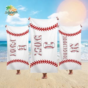May include: White baseball-themed beach towels with red stitching and text. Each towel features a name and number in a baseball font. The towels are displayed on a sandy beach under a bright sky.