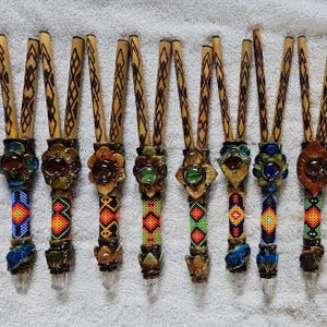 May include: A selection of handcrafted wooden smoking pipes. Each pipe has a floral design, colourful beaded accents, and a clear crystal tip. The wooden stems feature a carved pattern.