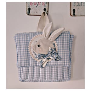 Peut inclure: Un sac de rangement en tissu à carreaux bleus et blancs avec un appliqué de visage de lapin. Le lapin a des oreilles crème et un nœud à motifs bleus et blancs. Le sac est conçu pour le rangement et a une texture matelassée.