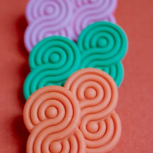May include: An assortment of colorful, abstract shapes in shades of pink, green, and orange. Each shape features a repeating, swirling pattern, set against a solid orange background. The shapes are arranged in a visually appealing composition.