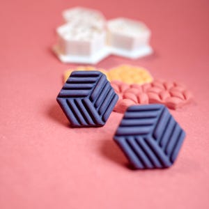 May include: Close-up of several colorful geometric shapes on a pink background. Two dark blue, hexagonal shapes with a striped design are in focus. Other shapes in white, yellow, and pink are blurred in the background.