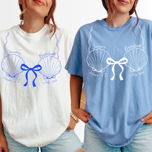 May include: Two t-shirts, one white and one light blue, featuring a seashell design with the text "Jessica's Bachelorette" and "Miami, FL July 2026". The design includes a bow and is printed in blue and white.