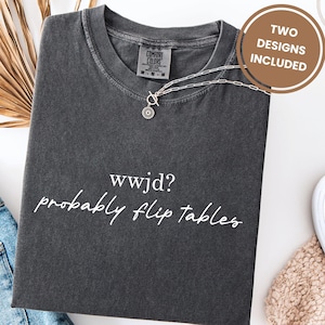 May include: A dark gray t-shirt with the text "wwjd? probably flip tables" in white script. A silver necklace with a sunburst pendant rests on the shirt. The words "TWO DESIGNS INCLUDED" are in a brown circle.
