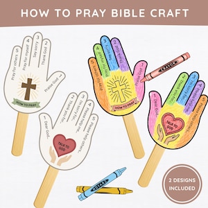 May include: A How to Pray Bible craft set featuring hand-shaped paper cutouts on wooden sticks. Two designs are shown: one with a cross and one with a heart, both labeled with numbered prayer steps. A pink crayon and a blue crayon are included.
