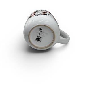 May include: A white ceramic mug featuring a Halloween-themed pattern with orange and black Minnie Mouse silhouettes, spiderwebs, and bats. The base displays the Disney logo, dishwasher safe text, and the Zrike Brands logo in black ink.