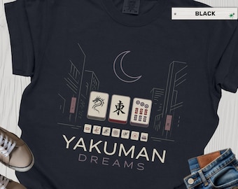 May include: Black t-shirt with a graphic design featuring three Mahjong tiles, a crescent moon, and city buildings. The text "YAKUMAN DREAMS" is printed below the tiles. The shirt is black.