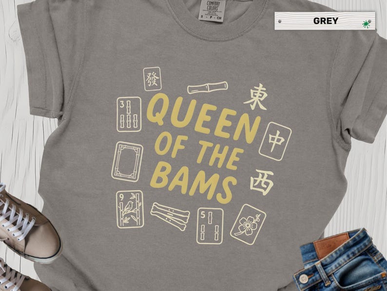 May include: A grey short-sleeved t-shirt featuring the text QUEEN OF THE BAMS in yellow lettering, surrounded by various Mahjong tile illustrations and Chinese characters printed in a light cream color on the front of the garment.